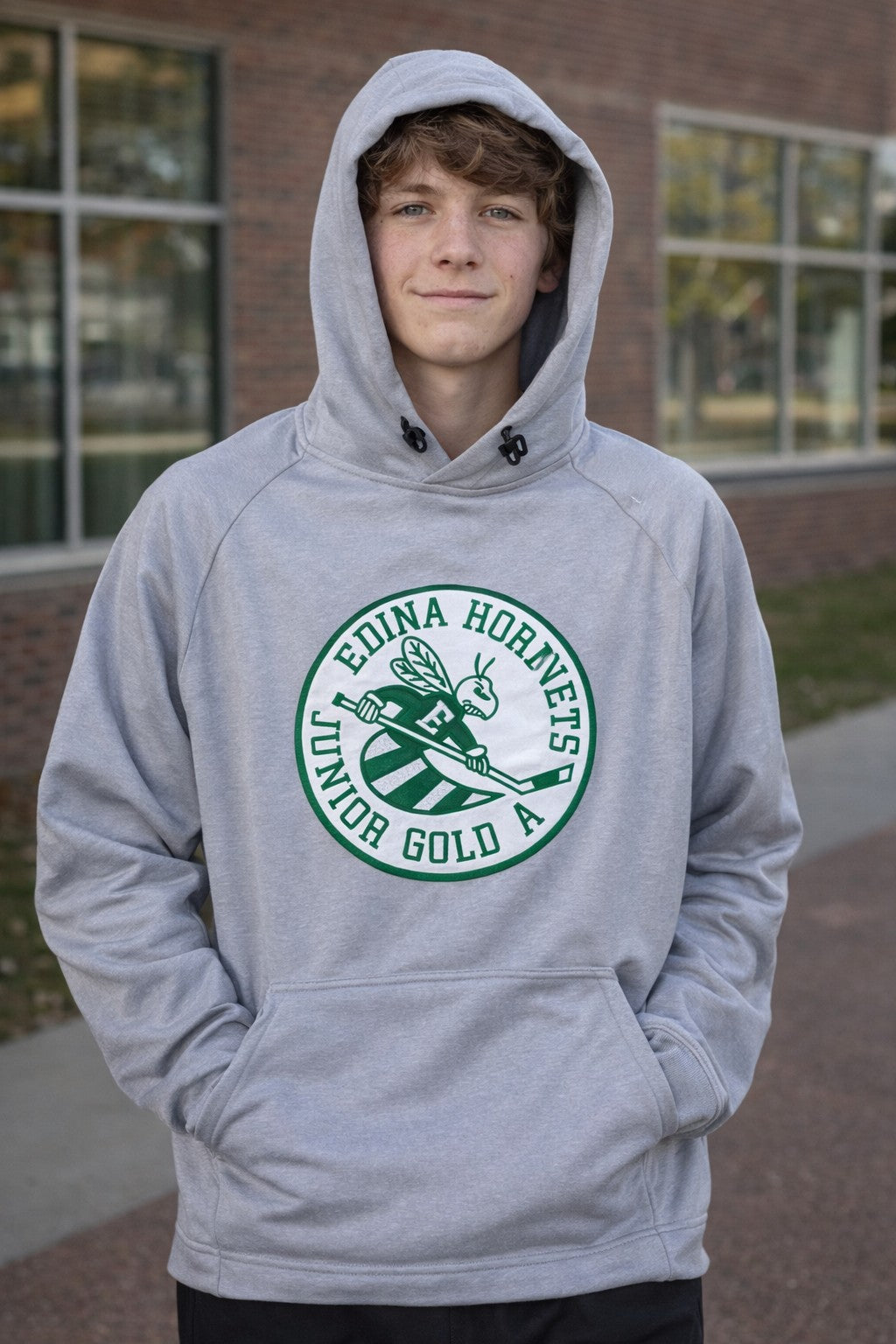 Person wearing a gray hoodie with a green and white logo in front of a brick building.