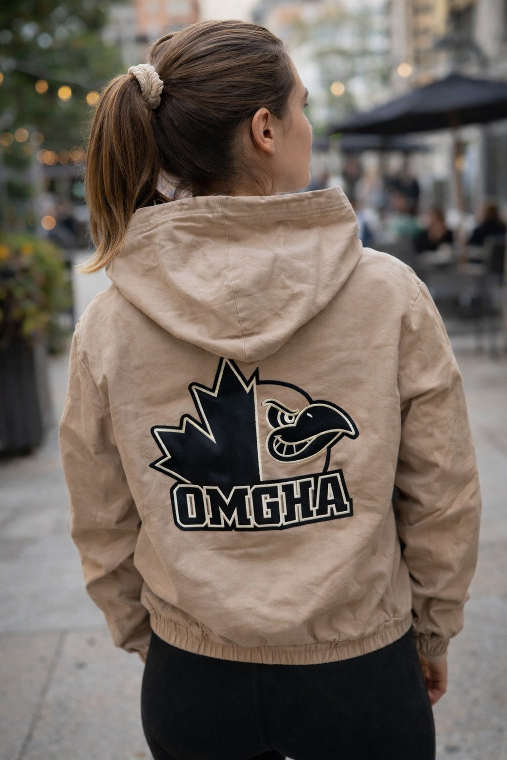 Person wearing a beige jacket with a logo and 'OMEGA' text on the back, standing outdoors. 